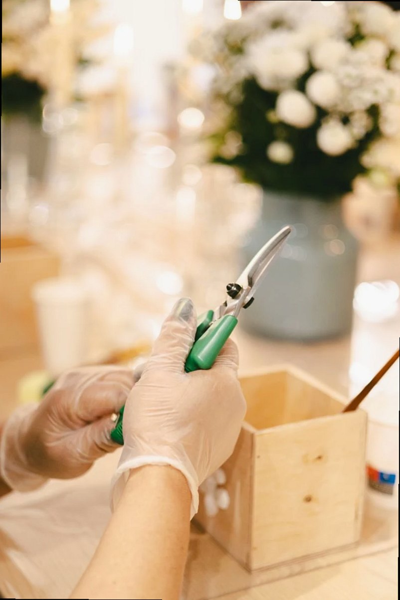Florista preparando un arreglo floral con tijeras de jardín, usando guantes para mayor precisión.