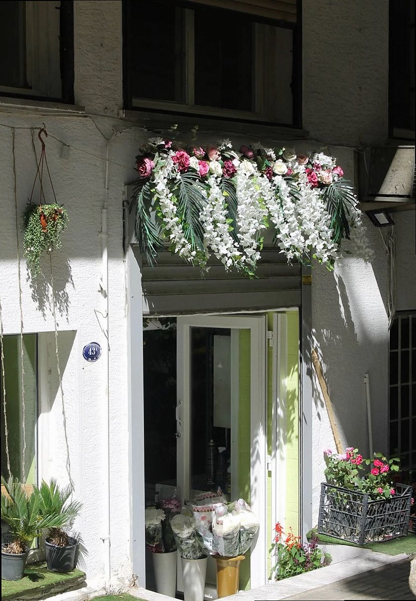 Entrada luminosa y acogedora de una floristería adornada con exuberantes arreglos florales en un entorno urbano.