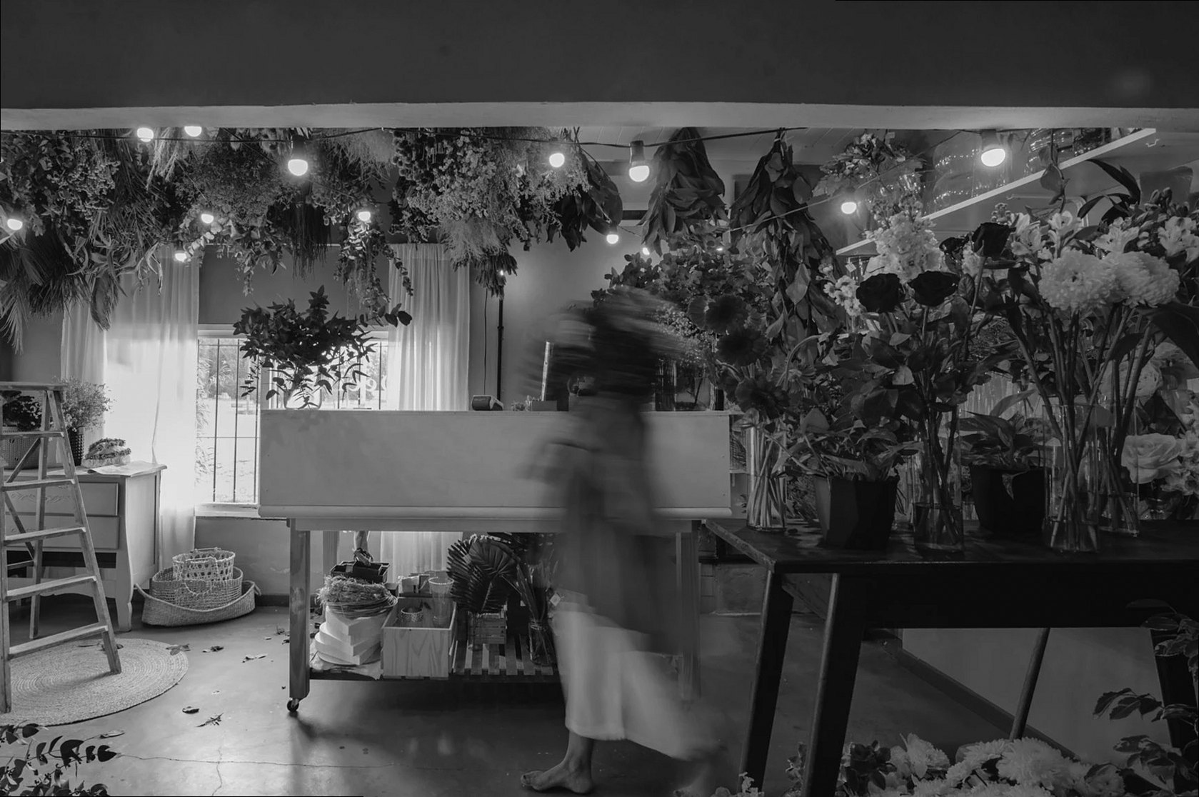 Una imagen monocroma de una floristería llena de diversas flores y una figura borrosa.