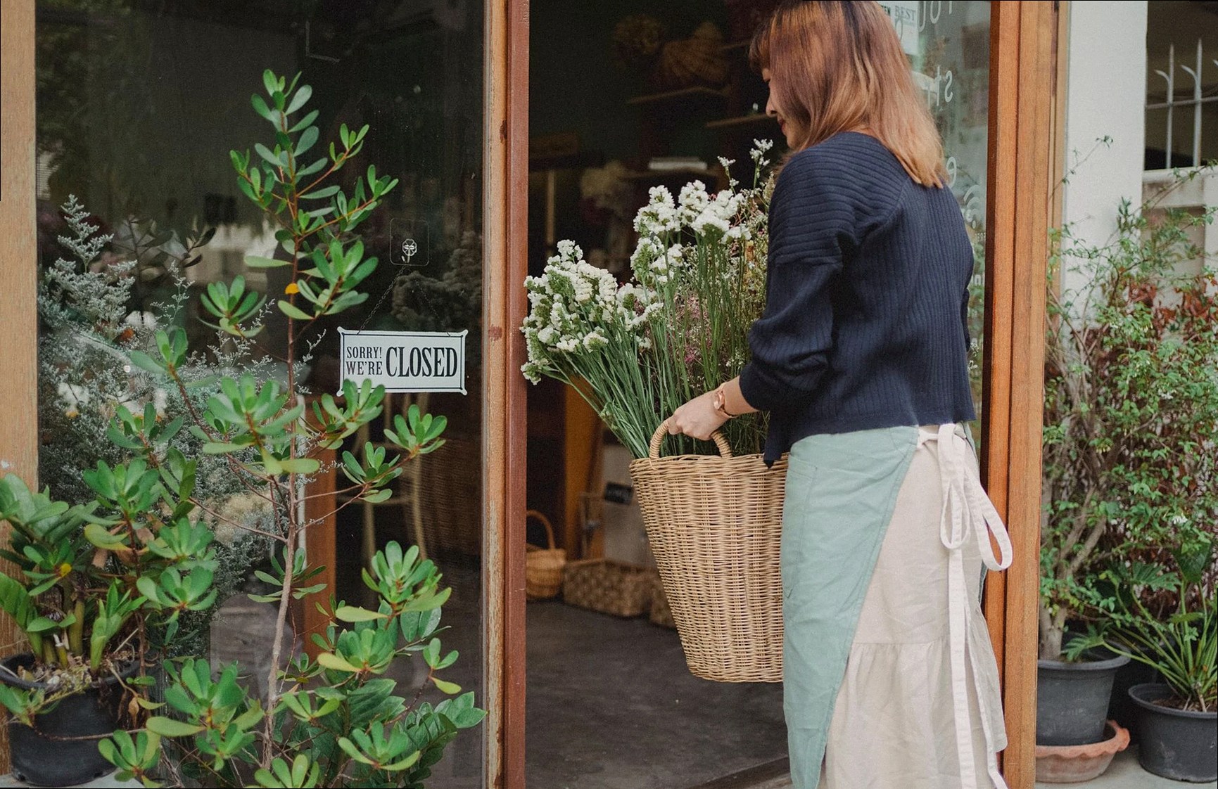 Florista con delantal llevando una cesta de mimbre con plantas a una floristería durante el día