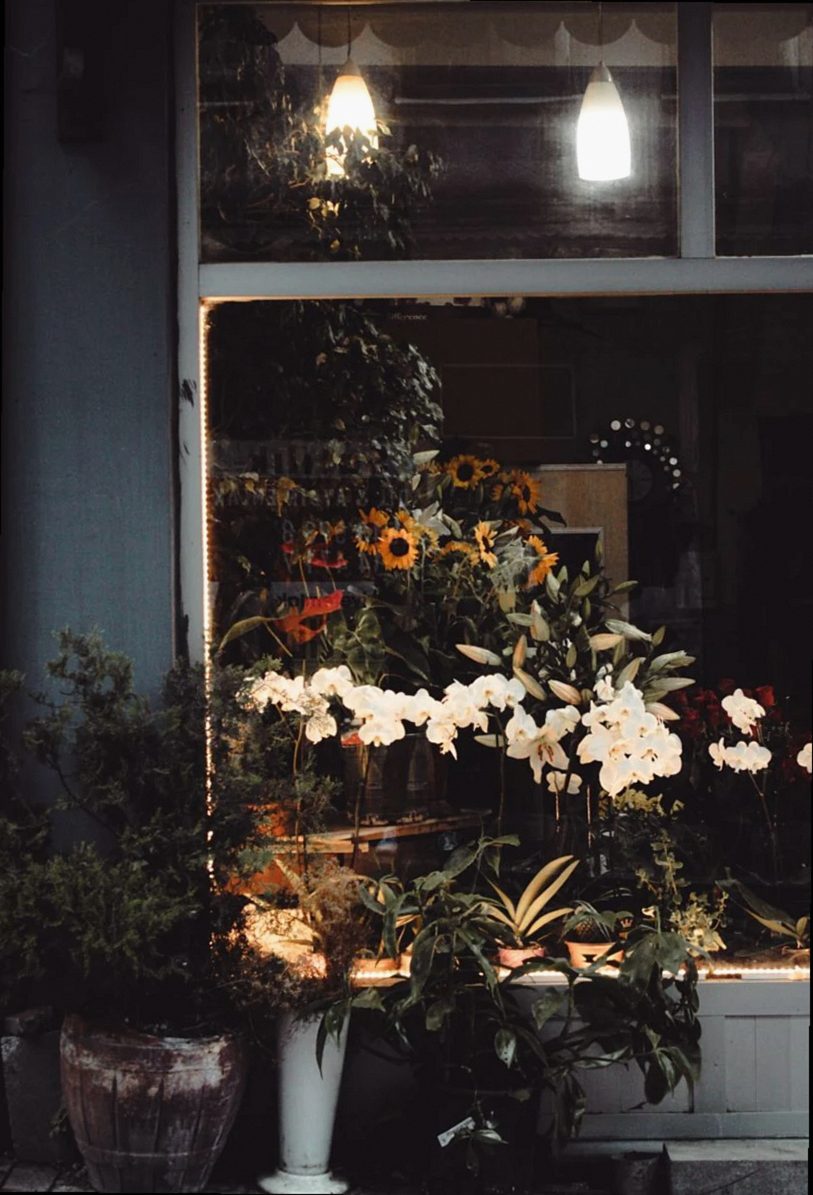 Elegantes arreglos florales en el escaparate de una floristería que brilla cálidamente por la noche.